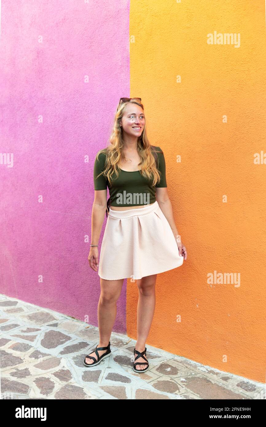 Jeune femme en robe se tient rire devant la maison colorée, orange et rose façade de maison, Burano Island, Venise, Vénétie, Italie Banque D'Images