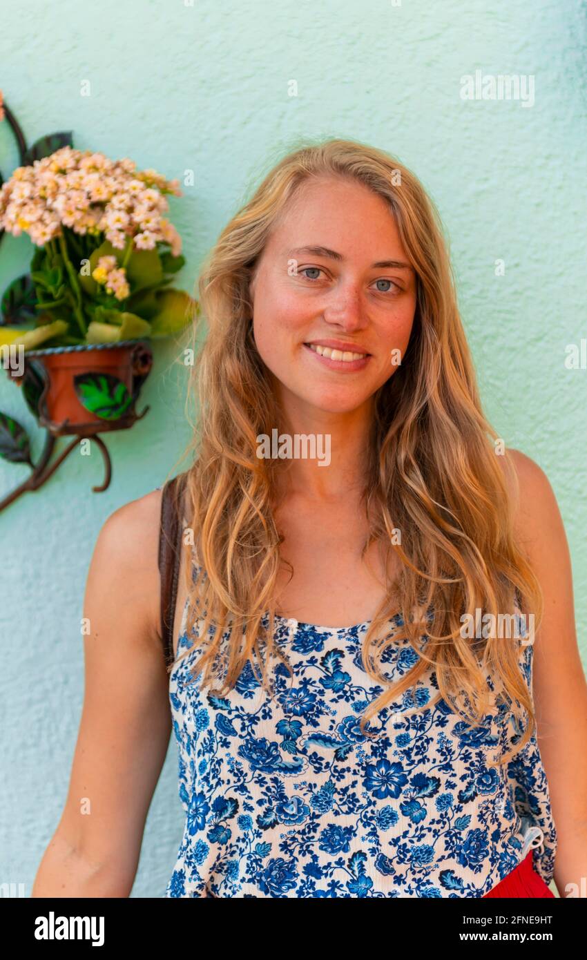 Jeune femme avec robe rouge devant le mur turquoise, île de Burano, Venise, Vénétie, Italie Banque D'Images