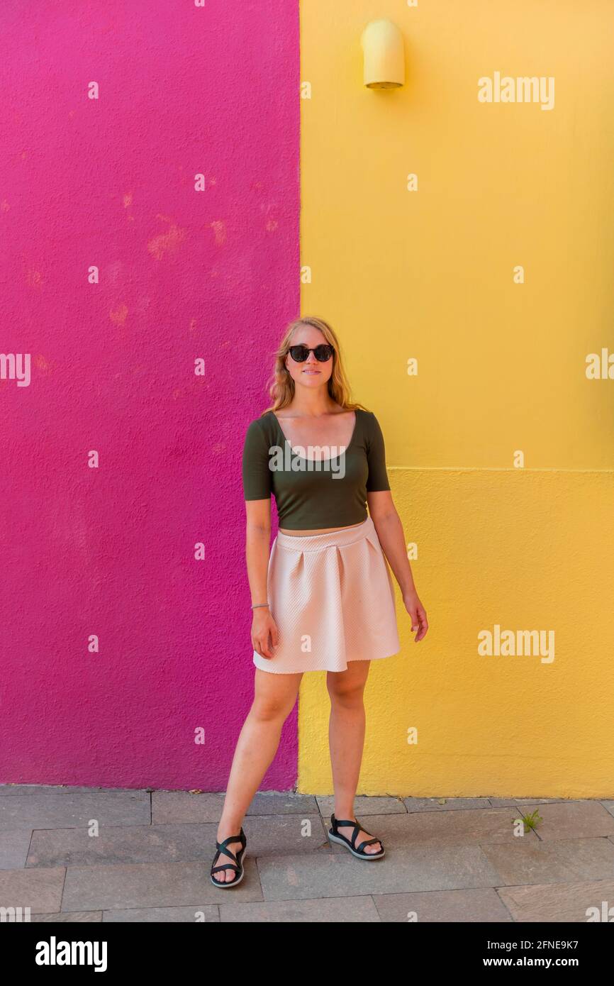 Jeune femme en robe se tient rire devant la maison colorée, jaune et rose façade de maison, Burano Island, Venise, Vénétie, Italie Banque D'Images