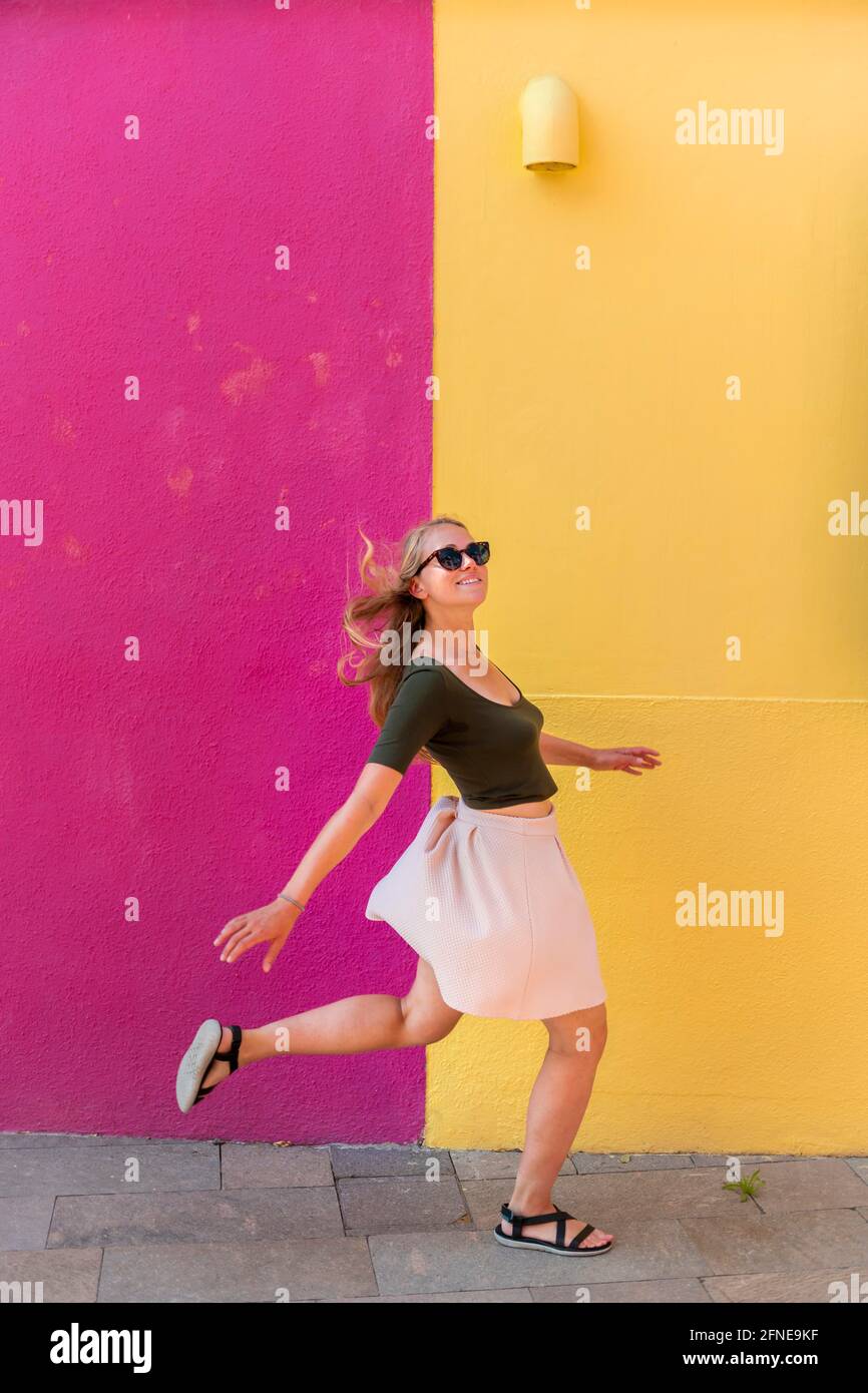 Jeune femme en robe saute heureusement devant la maison colorée, façade de maison jaune et rose, île de Burano, Venise, Vénétie, Italie Banque D'Images