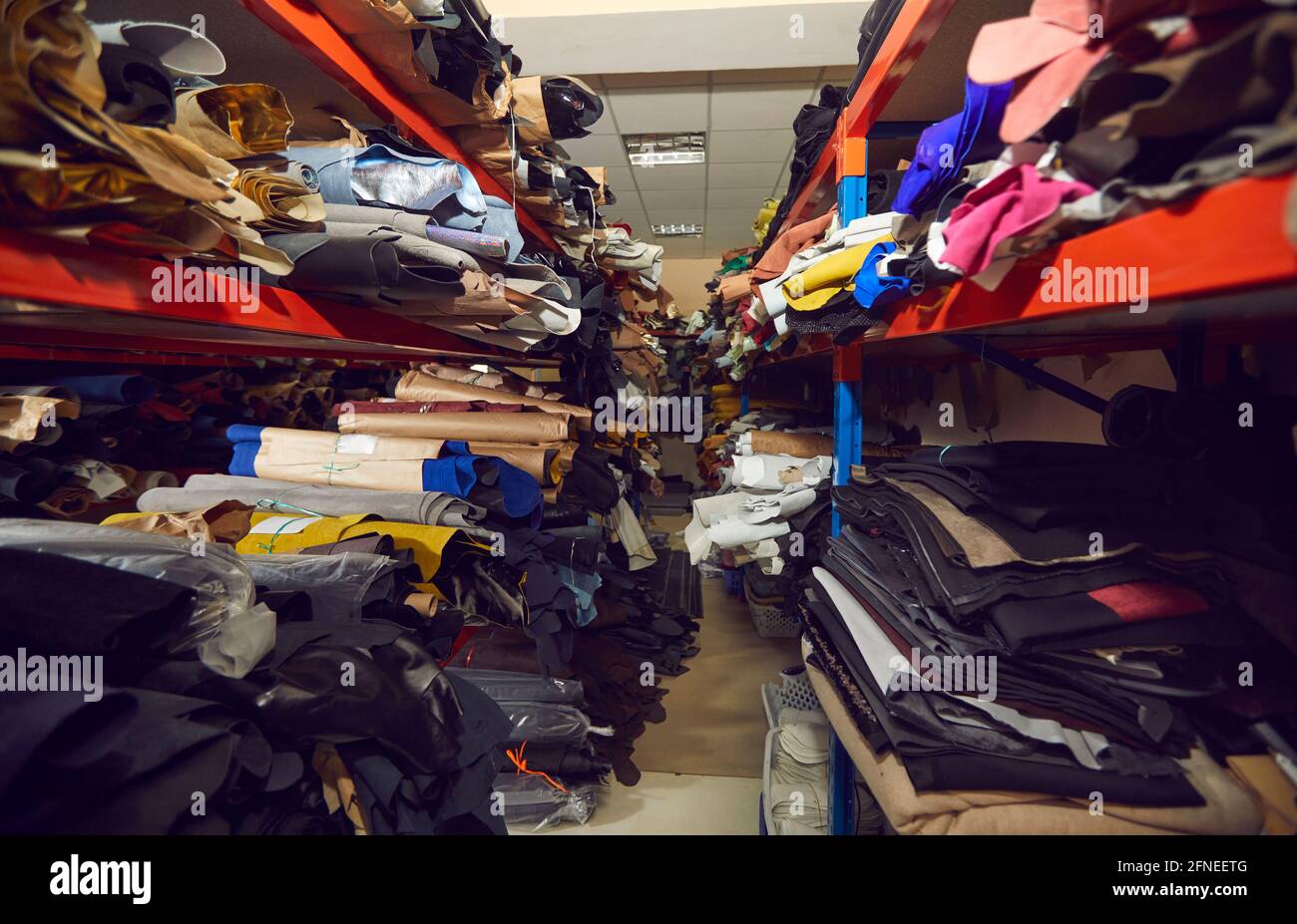 Allée entre les tablettes avec beaucoup de rouleaux de tissu et de cuir à l'usine de chaussures ou de vêtements Banque D'Images