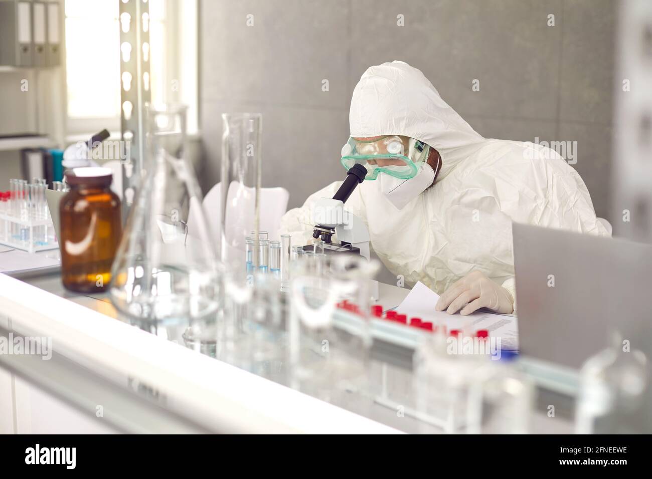 Scientifique dans le masque PPE et les lunettes de protection faisant la recherche et le travail avec microscope en laboratoire Banque D'Images