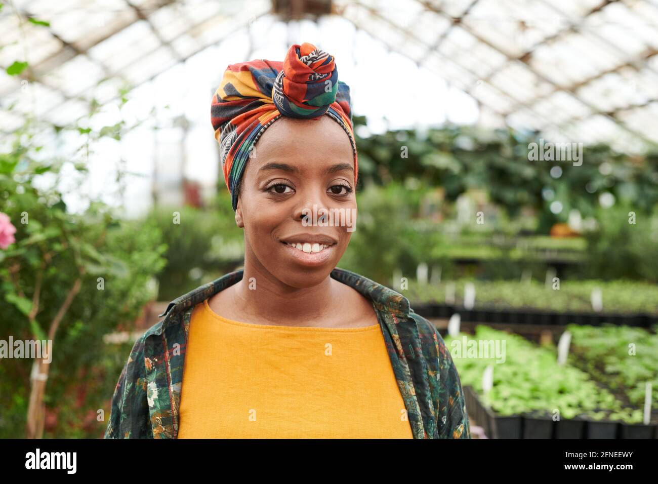Portrait d'une jeune femme africaine avec une coiffure colorée sur elle tête souriante à la caméra tout en travaillant en serre Banque D'Images