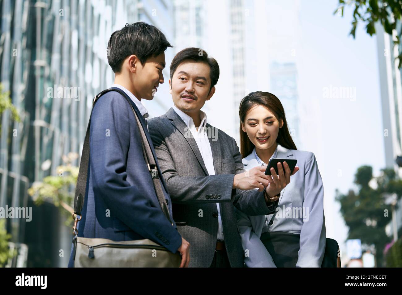 une équipe d'hommes d'affaires asiatiques debout dans la rue ayant une discussion en utilisant le téléphone cellulaire dans le centre-ville Banque D'Images