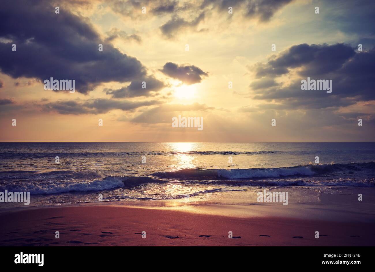 Plage tropicale avec empreintes de pieds dans le sable au coucher du soleil, couleurs appliquées. Banque D'Images