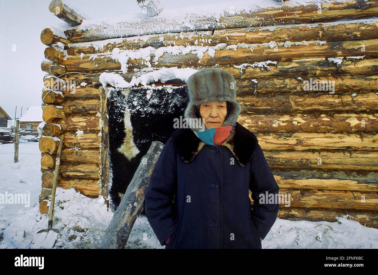 Vieille femme russe avec chapeau de fourrure devant une maison en bois. [traduction automatique] Banque D'Images