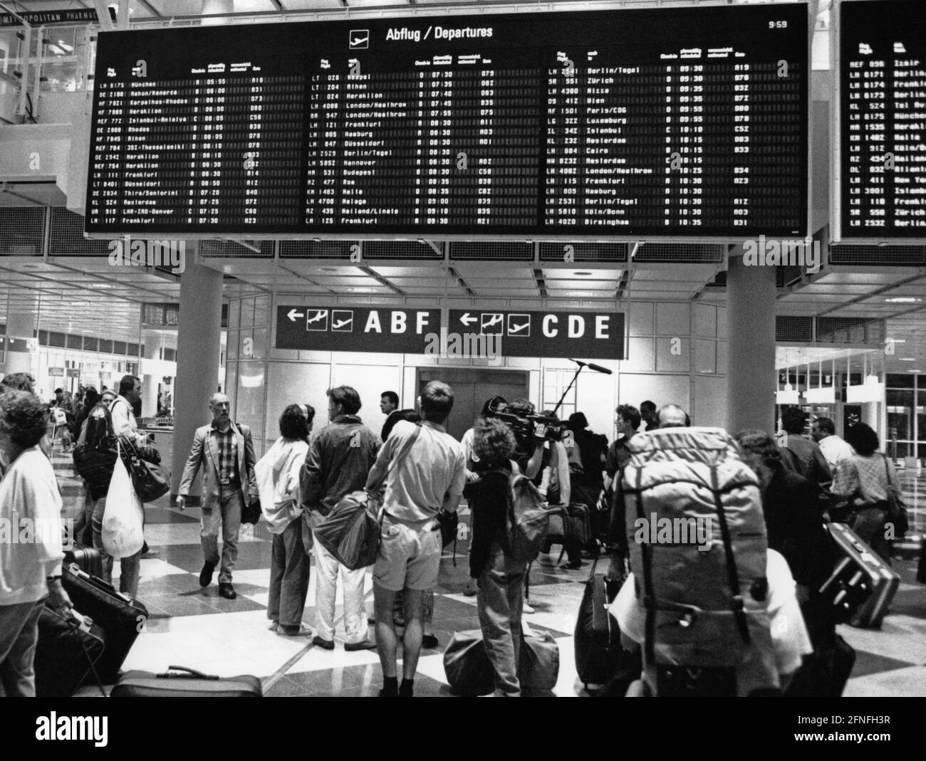 Devant un panneau d'affichage dans le terminal 1 de l'aéroport d'Erdinger Moos, les passagers s'orientent et attendent leur vol. [traduction automatique] Banque D'Images