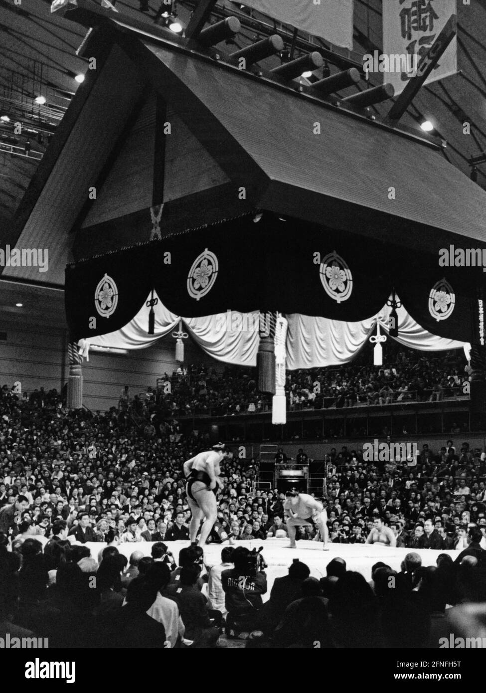 Vue à travers une salle à Osaka sur un combat de Sumo. Beaucoup de visiteurs regardent le combat. Deux combattants sumo sont prêts pour le combat sur le ring. Une construction de toit élaborée est construite sur les combattants et l'anneau. [traduction automatique] Banque D'Images