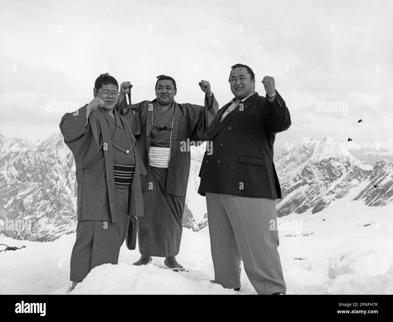 Trois lutteurs sumo se tiennent avec des poings levés au sommet du Zugspitze. En arrière-plan les Alpes. [traduction automatique] Banque D'Images