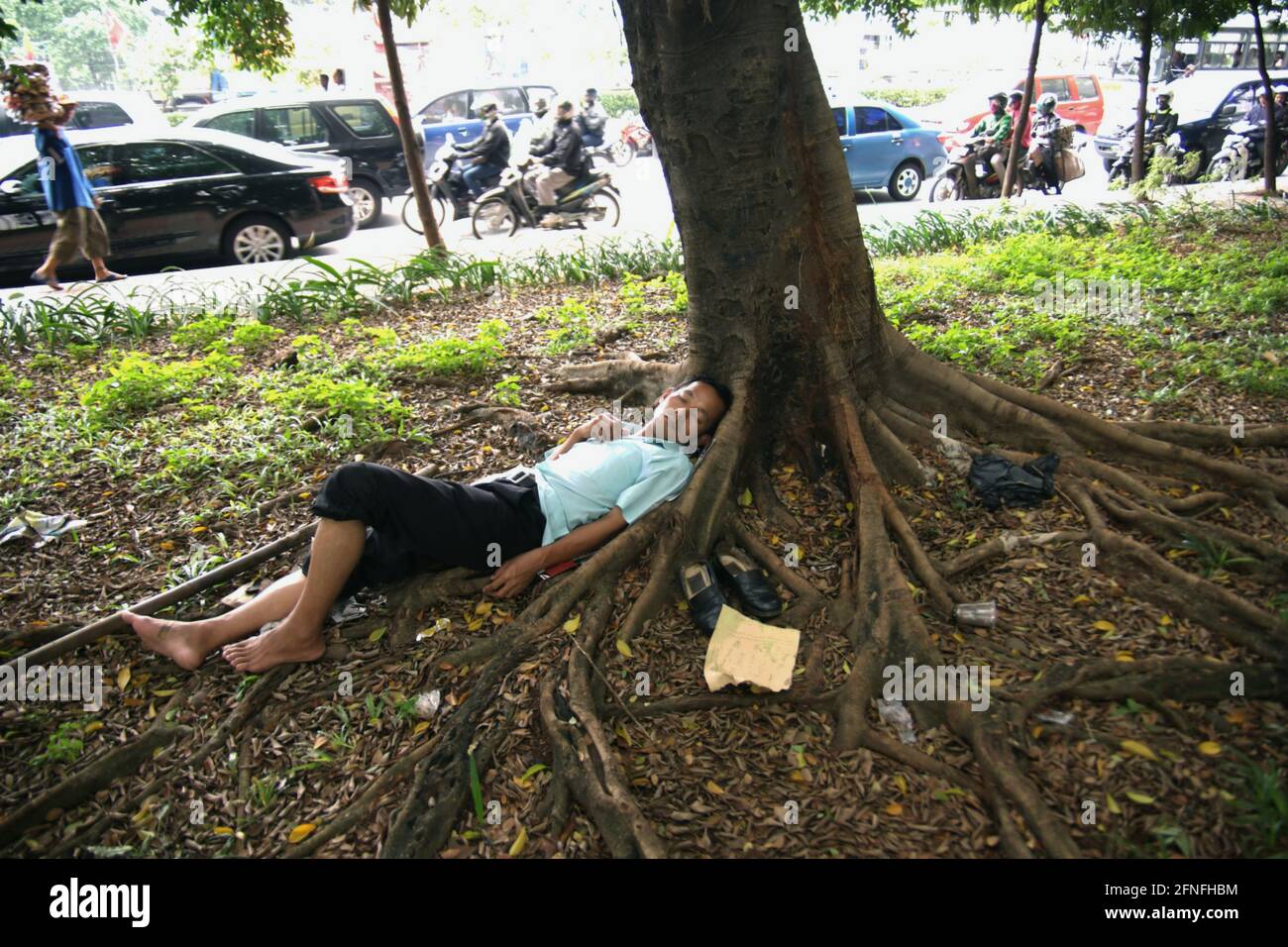 Un chauffeur de taxi avec compteur se dormant sous un arbre, photographié dans un contexte de circulation routière dense dans la région de Senayan, Jakarta, Indonésie. Banque D'Images