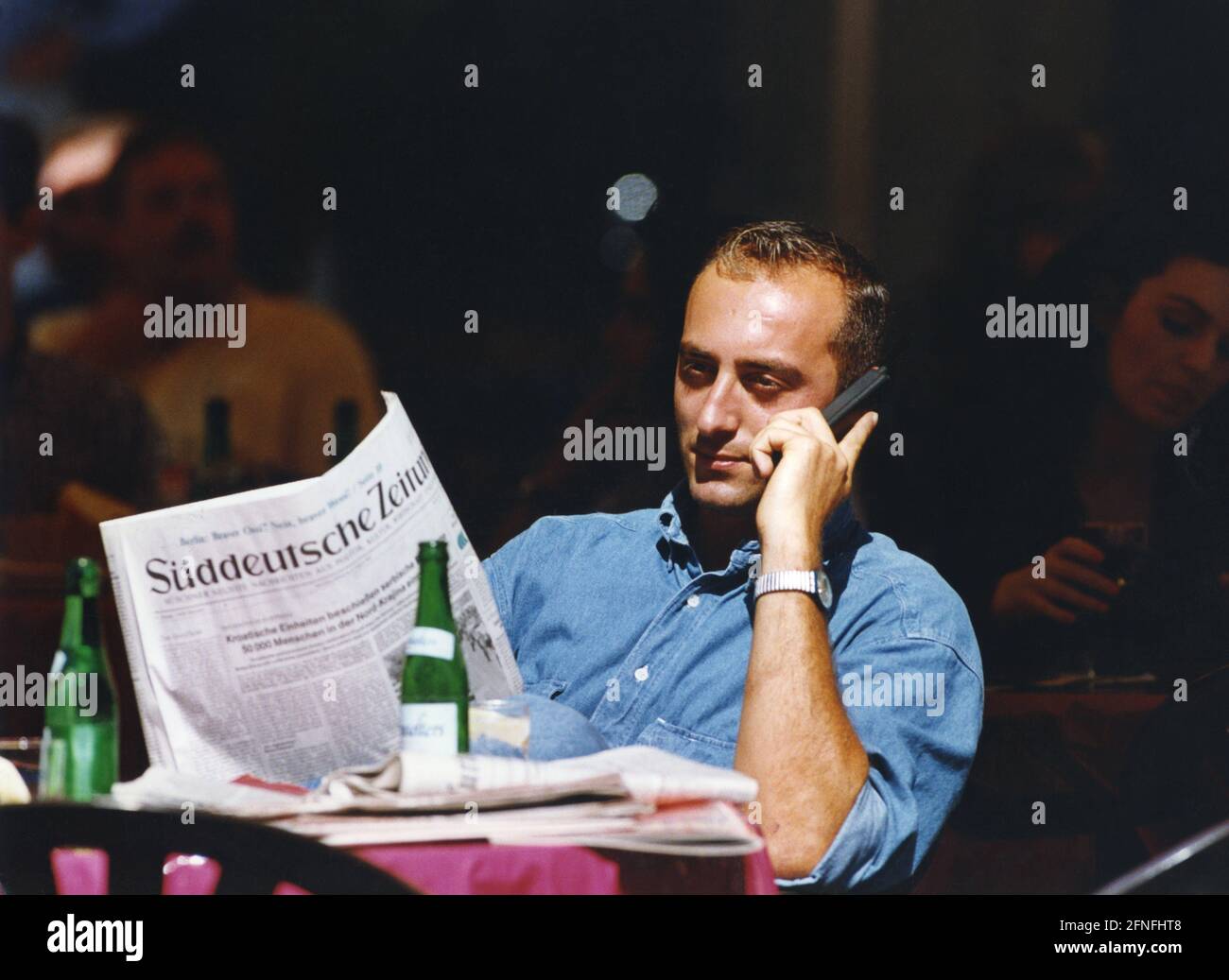 Homme parlant sur un téléphone portable et lisant le Süddeutsche Zeitung dans un café. [traduction automatique] Banque D'Images