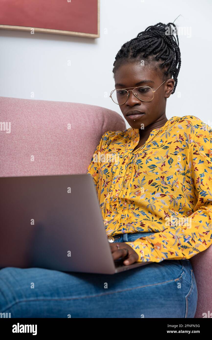 Femme indépendante afro-américaine concentrée assise sur un canapé à la maison et de taper sur netbook tout en travaillant sur le projet Banque D'Images