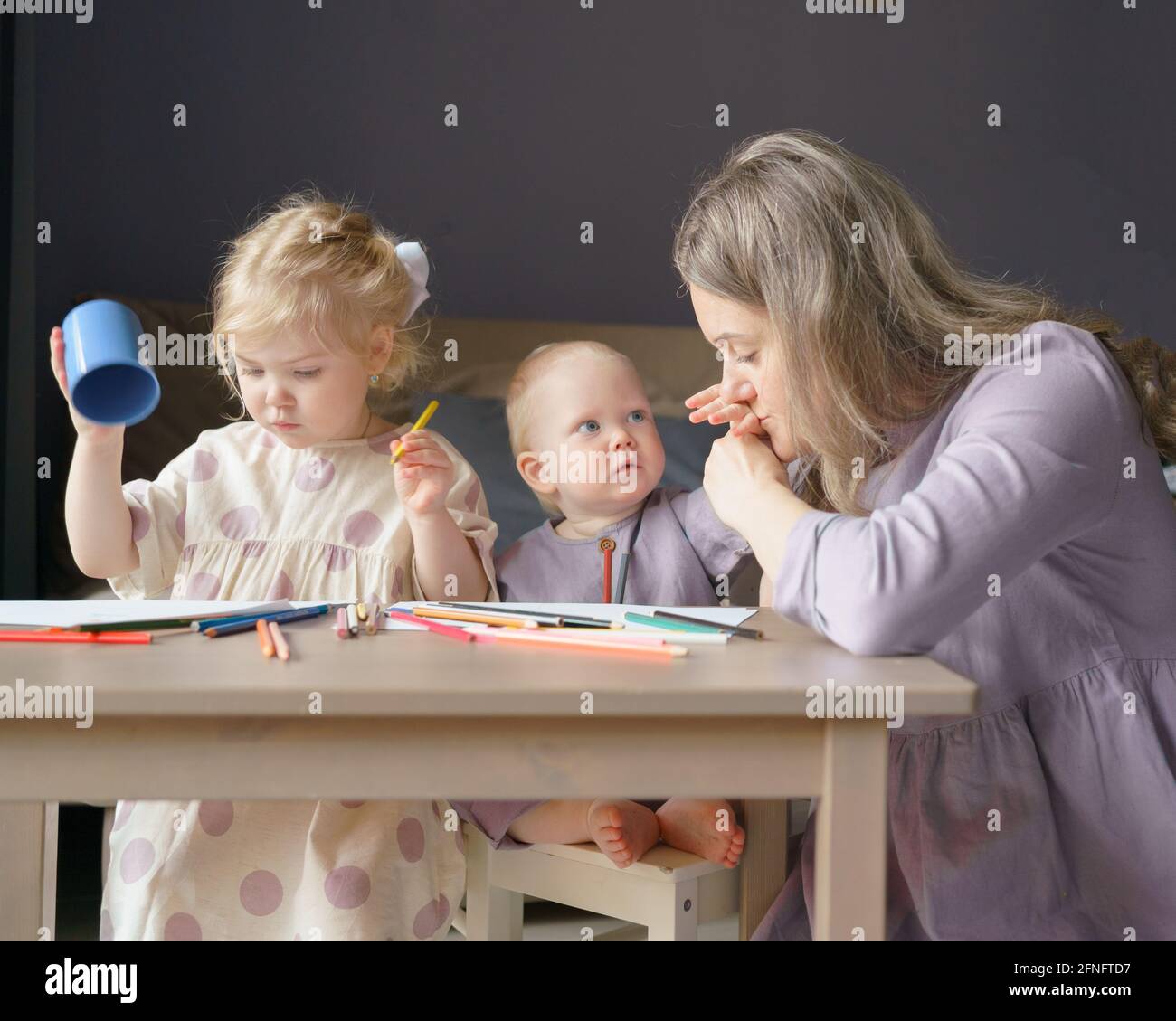 Une jeune mère aimante embrassant la main de son fils adorable bébé garçon avec des yeux bleus et des cheveux dorés tout en dessinant avec des enfants soeur plus âgée et petit frère à la maison, la famille maman et les enfants effectuant des activités artistiques Banque D'Images