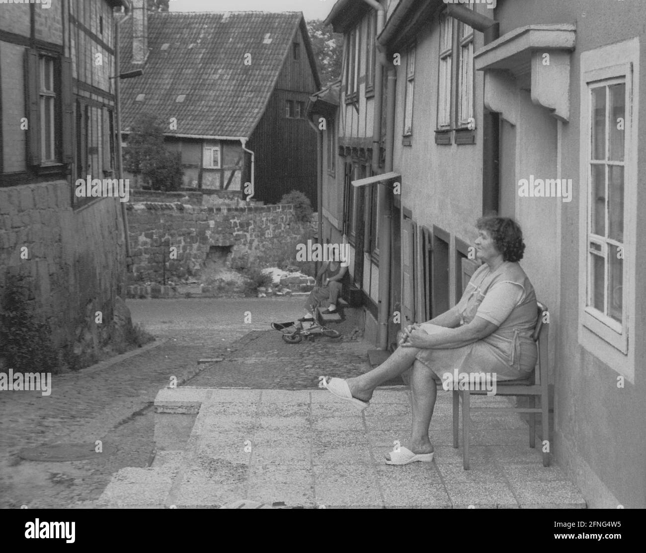 Saxe-Anhalt / GDR Land / 1990 Quedlinburg, cité impériale médiévale: Vieille ville à la collégiale, les femmes assis devant les appartements dans la soirée // personnes / Quedlinburg est devenu un palais impérial en 919, après l'élection du premier roi allemand, le duc saxon Heinrich. Son fils, Otto Ier, fit construire un monastère féminin sur le site du palais en 936. Dans la collégiale, construite depuis 1100, le célèbre Trésor de la cathédrale est conservé. Il a été volé par les Américains après la dernière guerre et racheté par la famille du voleur en 1993 pour 3 millions d'euros. La cathédrale fait partie du Banque D'Images