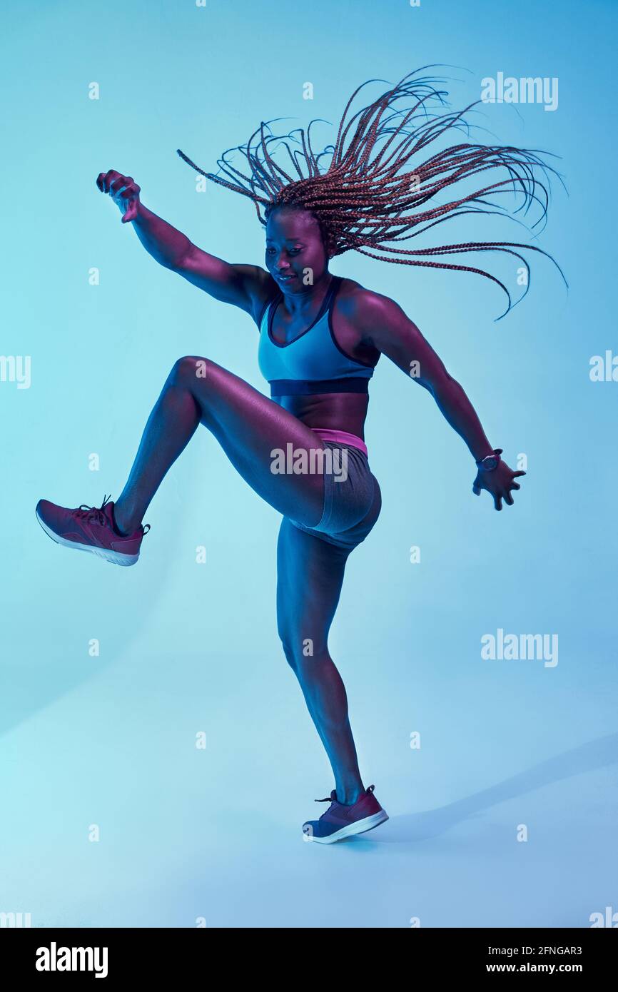 Forte athlète afro-américaine dans les vêtements de sport avec l'Afro volant braïdes et biceps regardant dans la lumière de néon Banque D'Images