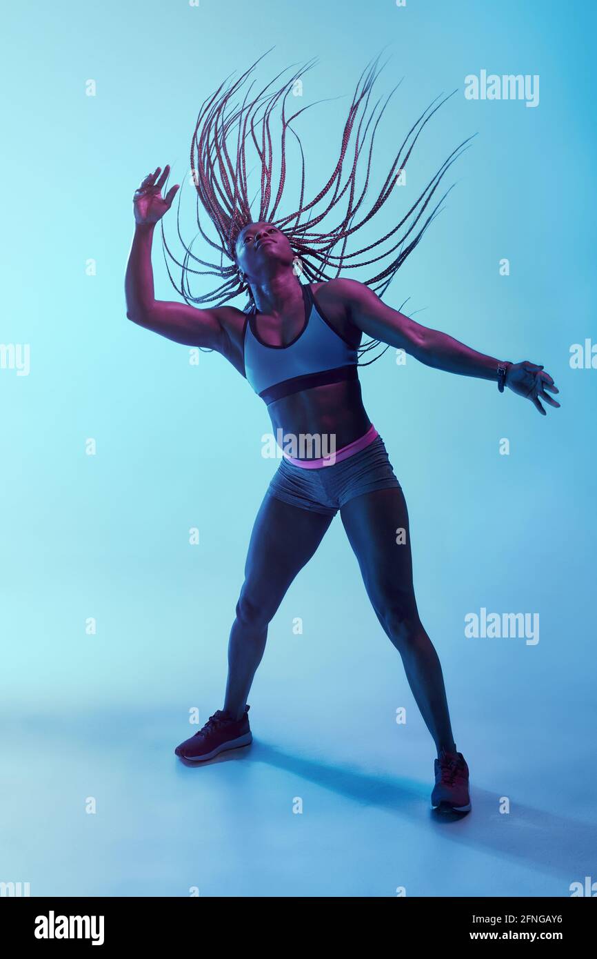 Forte athlète afro-américaine dans les vêtements de sport avec l'Afro volant braïdes et biceps regardant dans la lumière de néon Banque D'Images