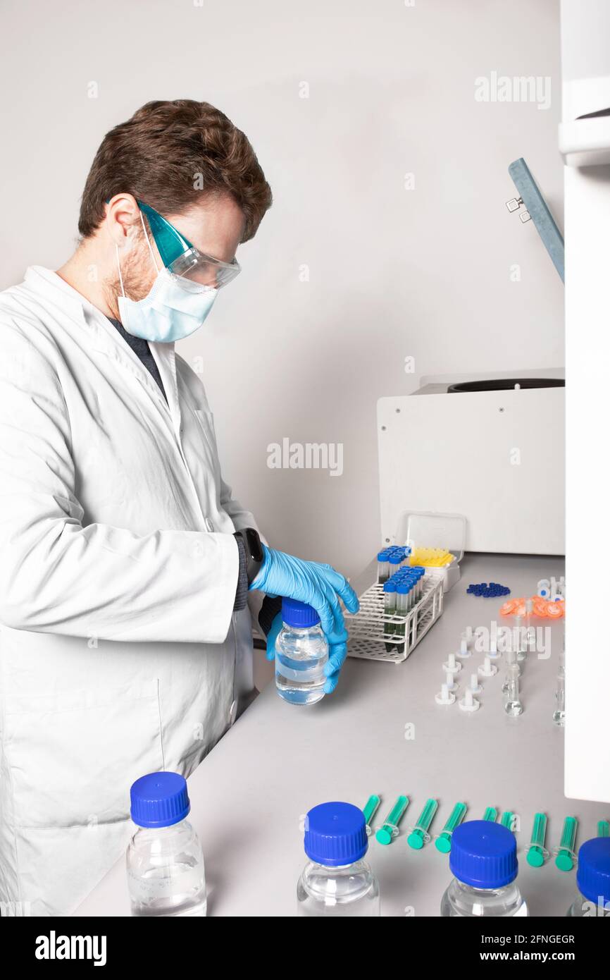 Vue latérale d'un biologiste masculin dans des lunettes et un masque de protection flacon d'ouverture avec liquide à la table dans le laboratoire de cannabis Banque D'Images