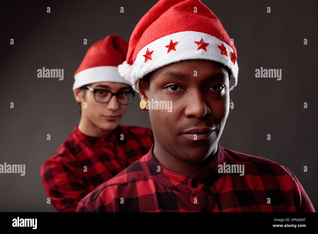 Des jeunes amis joueurs portent des chapeaux de père Noël rouges et colorés Célébrez la saison de Noël en souriant tranquillement à l'appareil photo ils se reflètent les uns les autres e Banque D'Images