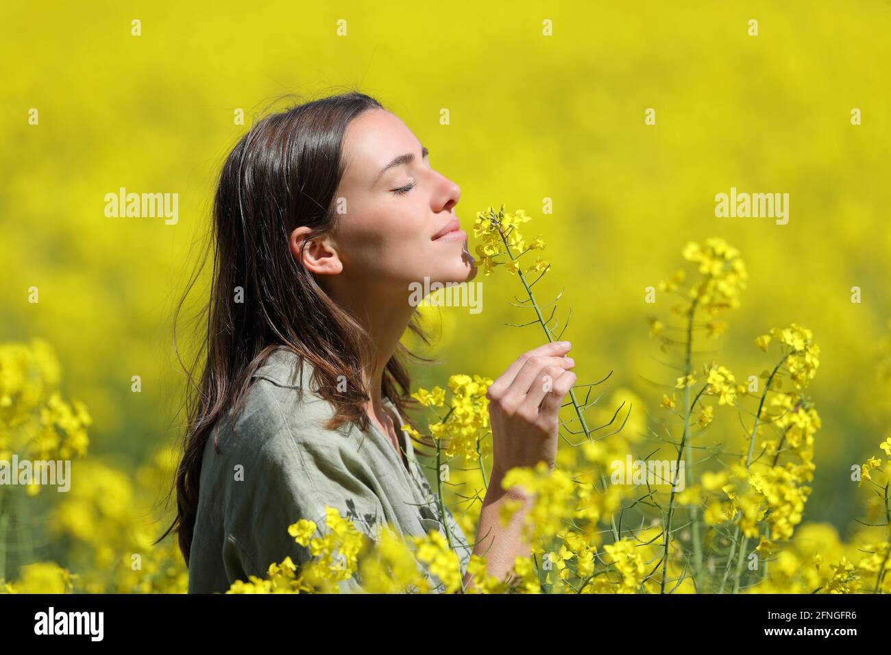 Profil d'une femme qui sent des fleurs dans un champ jaune Banque D'Images