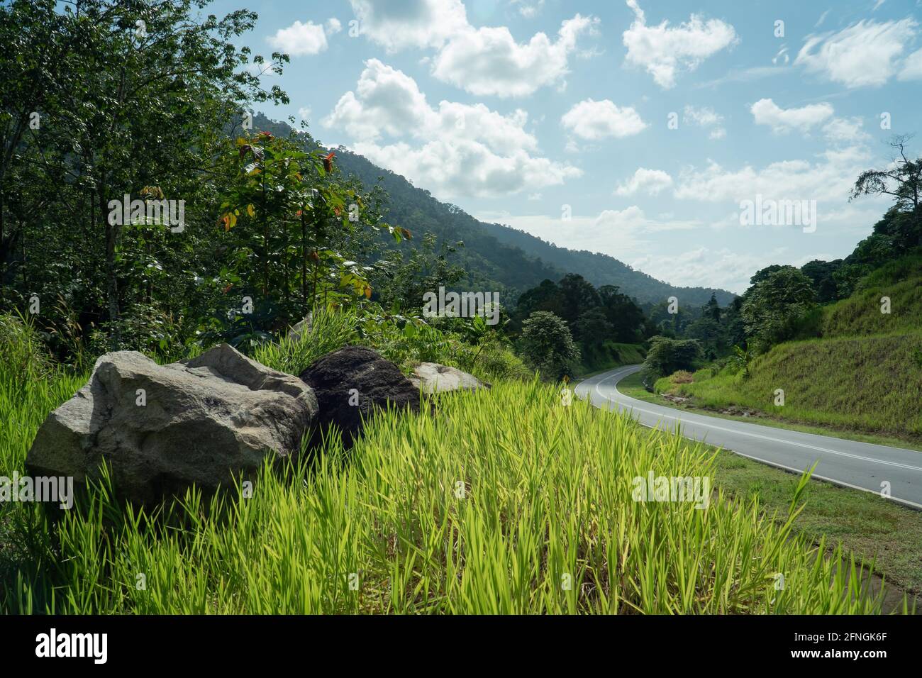 Paysage route de montagne. Route vide dans les hautes terres avec de l'herbe belle, pierre rocheuse et ciel bleu nuageux, Semenyih, Malaisie. Banque D'Images