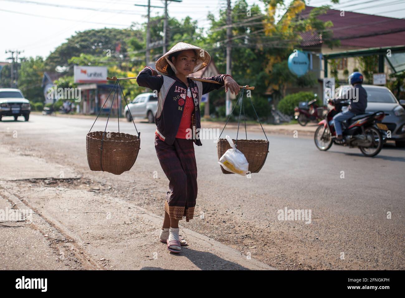 Pakse, Laos - 2 avril 2013 : une femme non identifiée portant des paniers avec de la nourriture. Banque D'Images