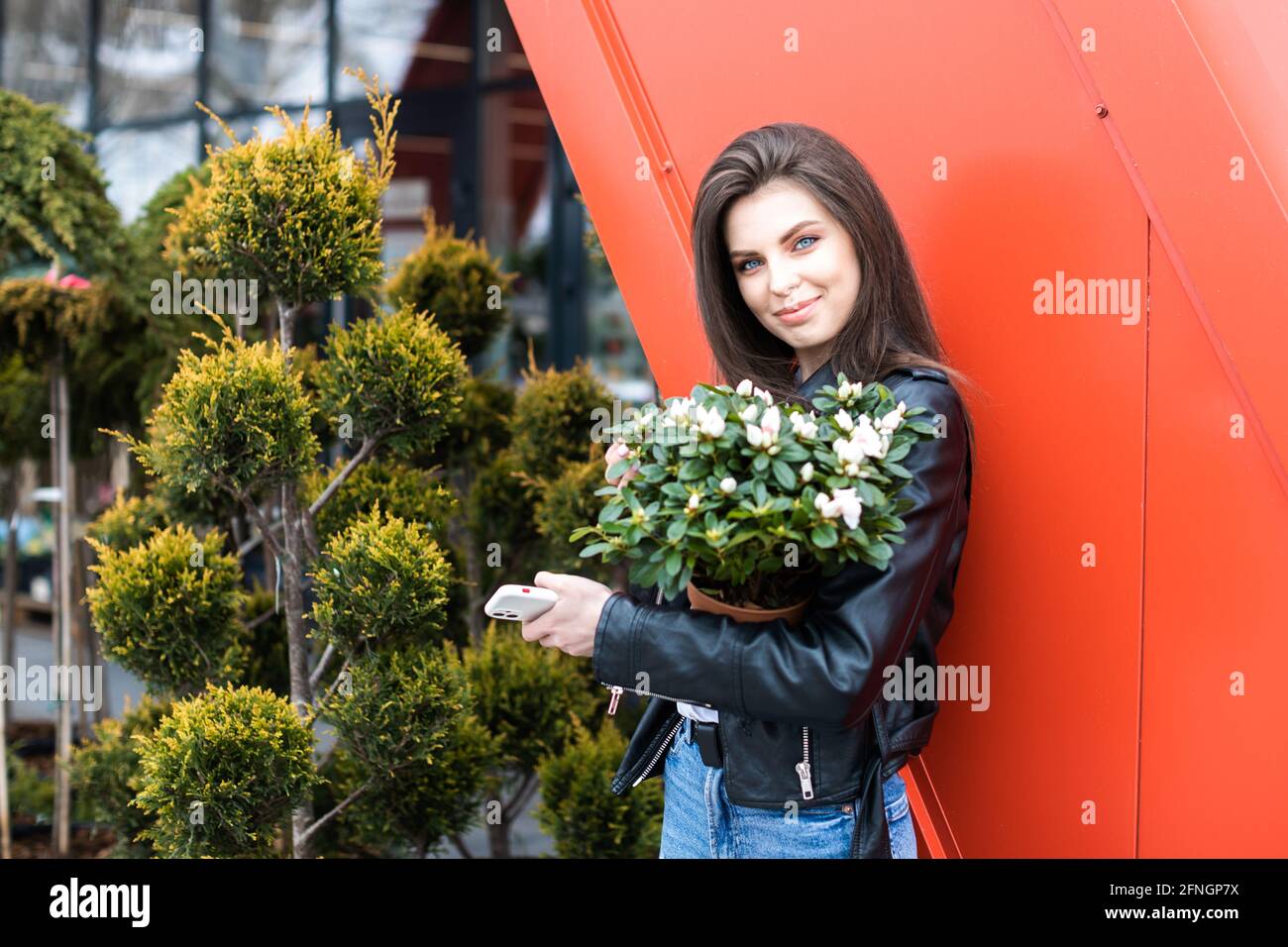 Une jeune jolie fille, vêtue d'une veste en cuir et d'un Jean, se tient près du centre de la fleur et tient un grand beau pot de fleurs Banque D'Images