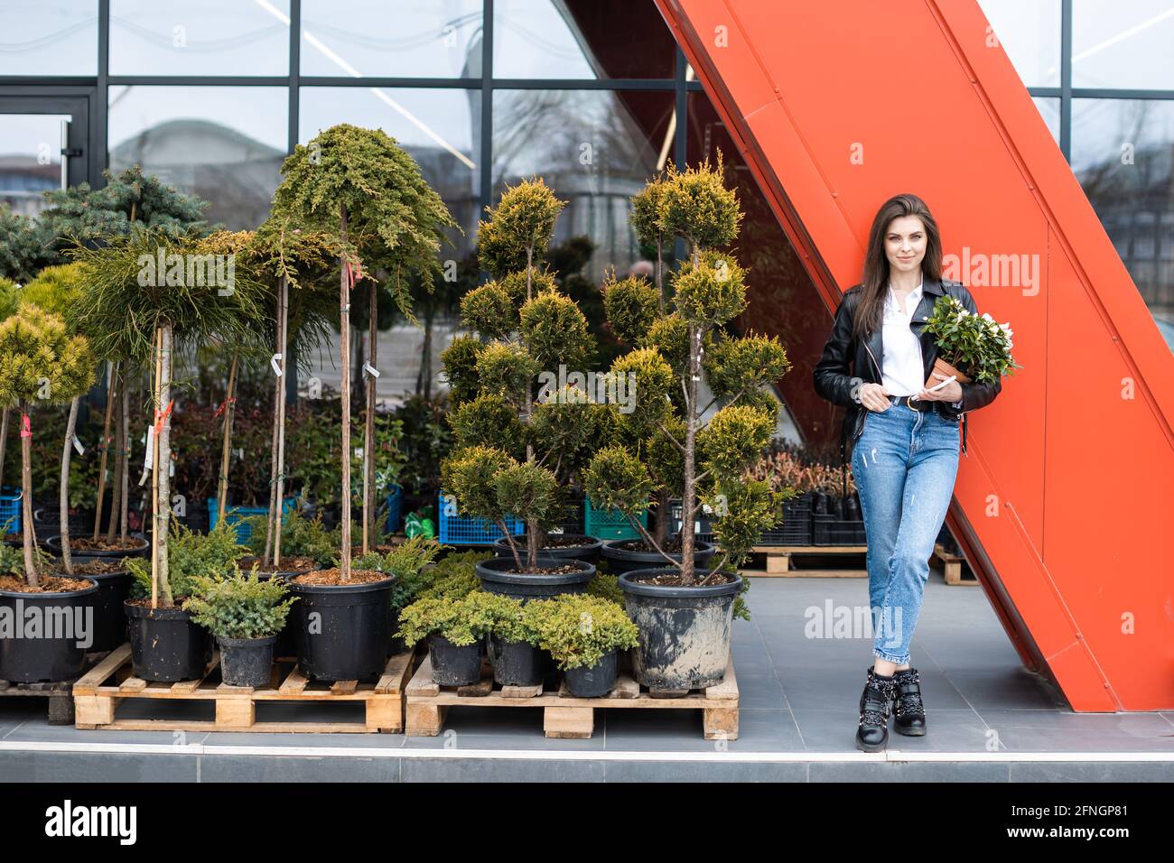 Une jeune jolie fille, vêtue d'une veste en cuir et d'un Jean, se tient près du centre de la fleur et tient un grand beau pot de fleurs Banque D'Images