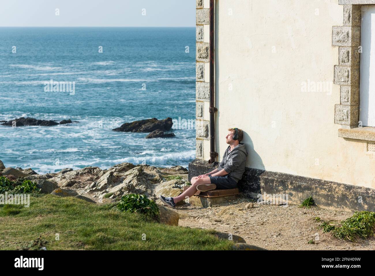 Un homme se détendant avec ses yeux fermés et assis contre l'ancienne station de Lifeboat à Little Fistral à Newquay en Cornouailles. Banque D'Images