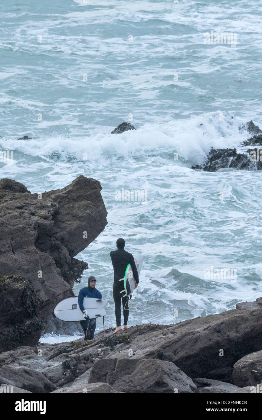 Surfeurs transportant leurs planches de surf et se tenant sur des rochers à la recherche d'une zone de lancement sûre en mer rugueuse à Little Fistral à Newquay, en Cornouailles. Banque D'Images