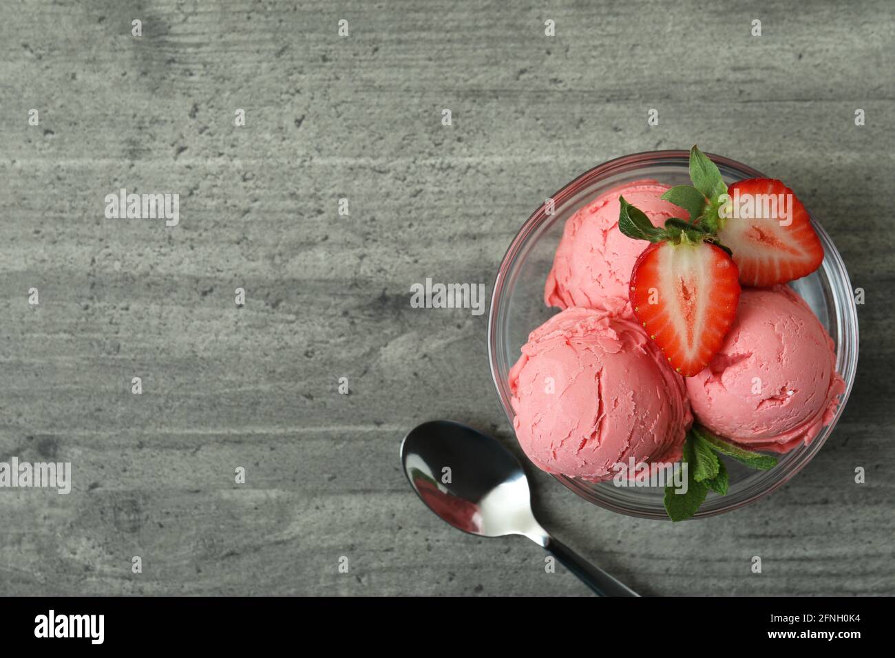 Bol avec boules de glace à la fraise sur table texturée grise Banque D'Images