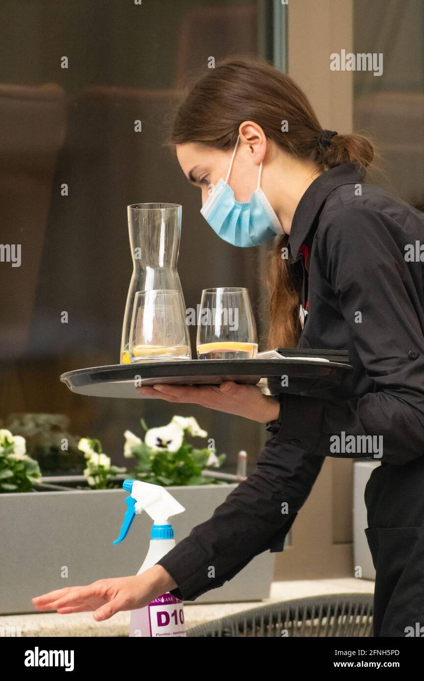 Jolie serveuse avec un masque qui nettoie, nettoie et désinfecte la table d'un bar extérieur, café, restaurant, rouvrant après verrouillage Banque D'Images