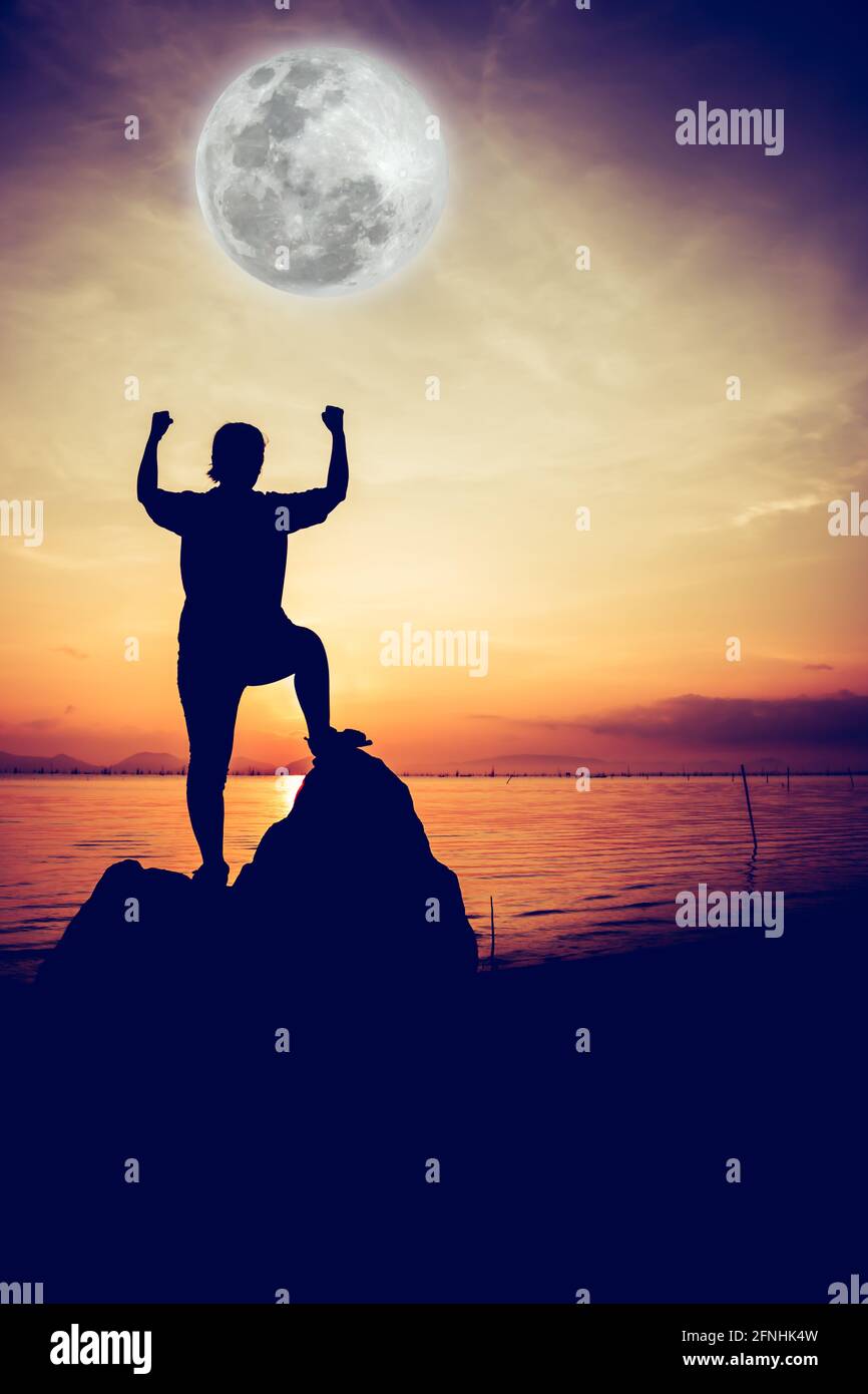 Silhouette de femme réussie se détendre et montrer bras vers le haut geste au bord de la mer sur fond clair de ciel pleine lune. Action du gagnant. Vignette styl. Image Banque D'Images