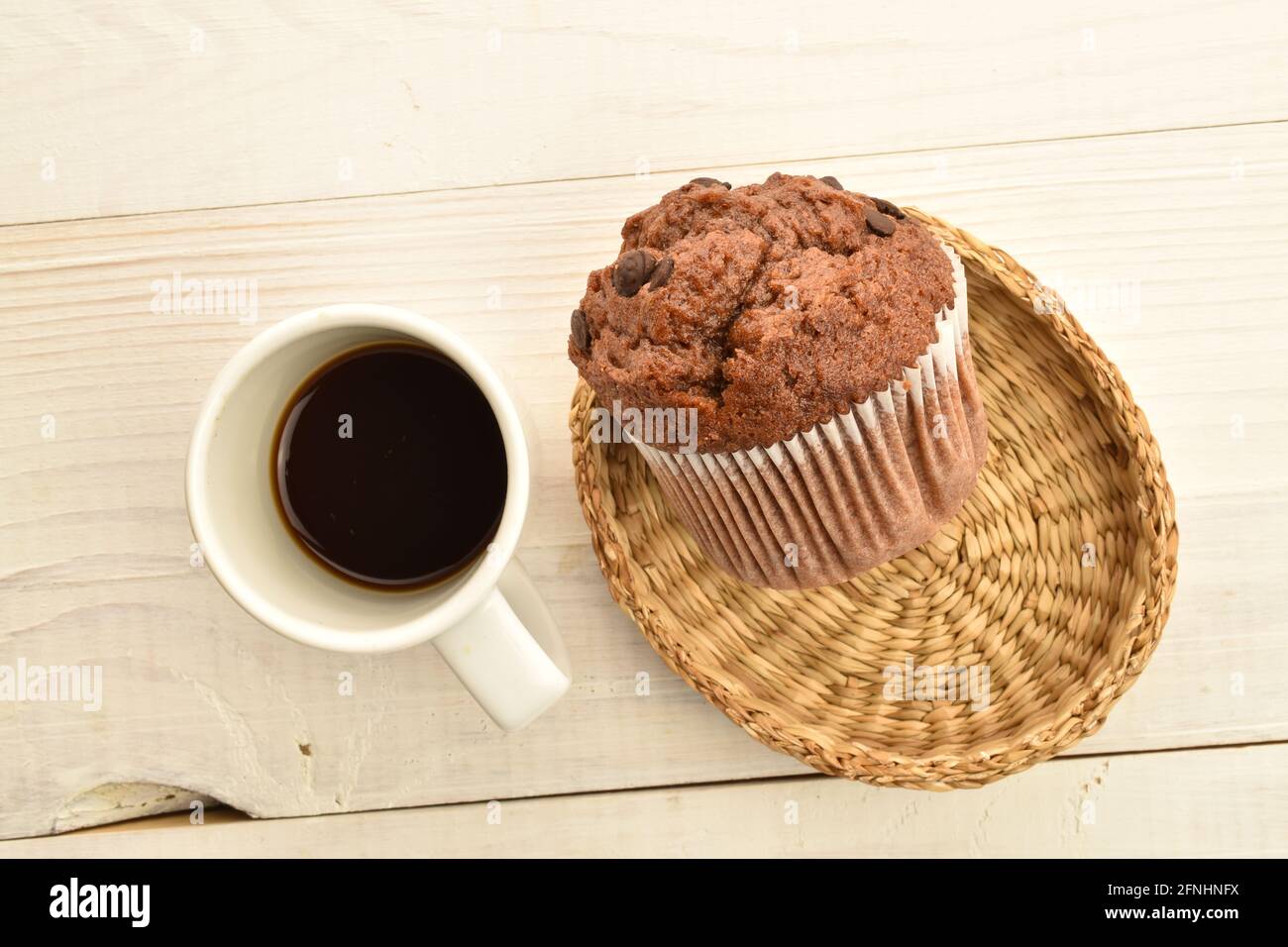 Un muffin au chocolat sur une assiette de paille avec une tasse de café, gros plan, sur une table en bois blanc, vue du dessus. Banque D'Images