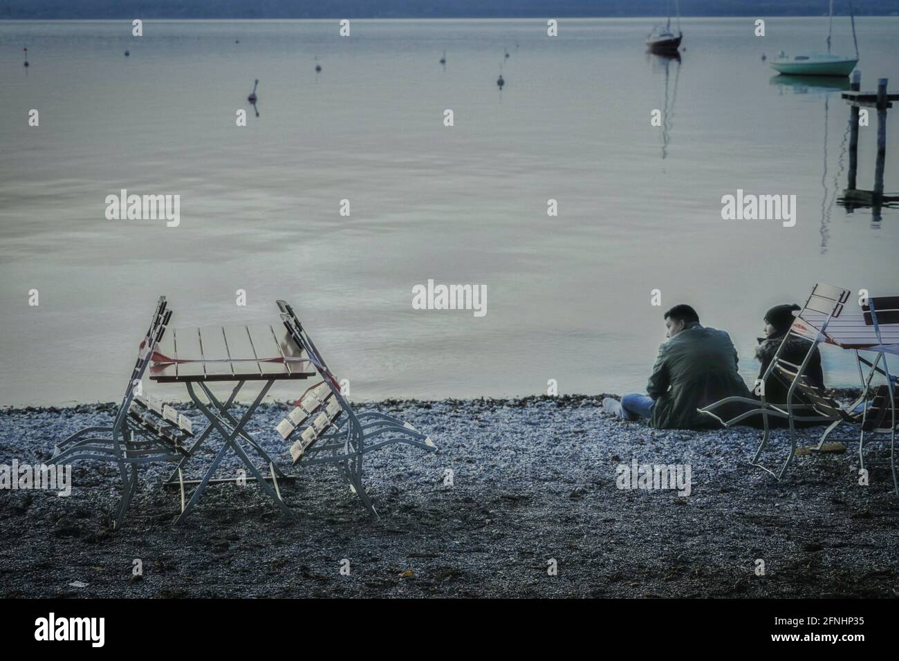 Un jeune couple se trouve sur une plage de galets d'un lac, sur le terrain d'un restaurant en plein air fermé pendant la pandémie de Corona. Banque D'Images
