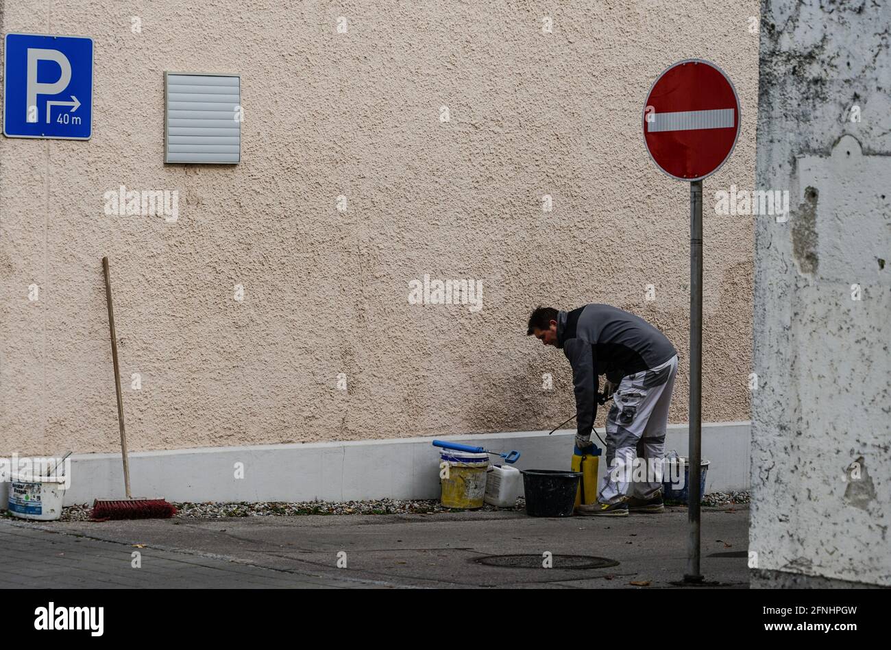 Un peintre se tient plié avec des seaux de peinture et d'outils devant un mur de maison qui doit être peint. Banque D'Images