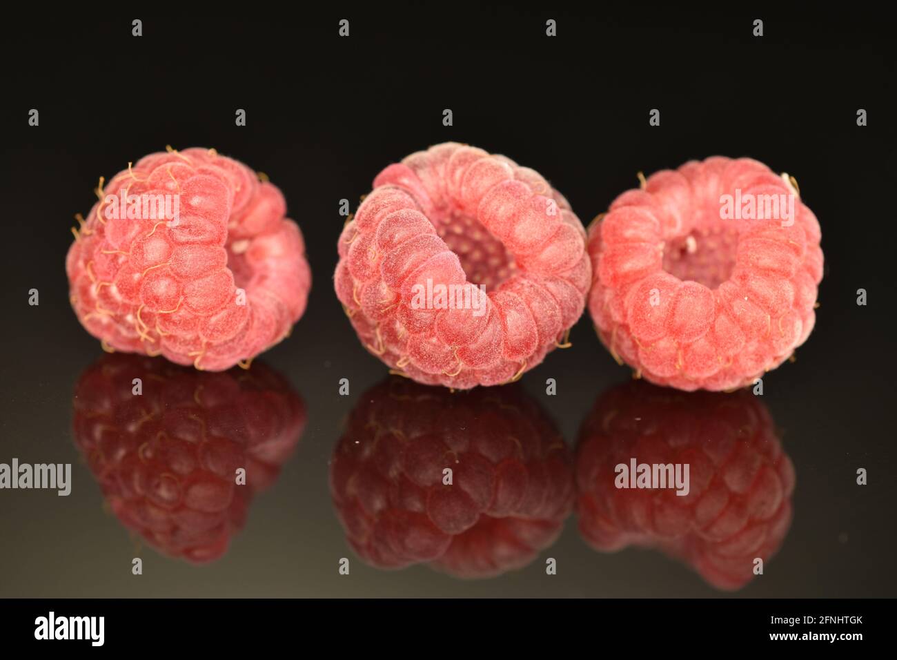 Trois framboises mûres rouges, en gros plan, isolées sur le noir. Banque D'Images