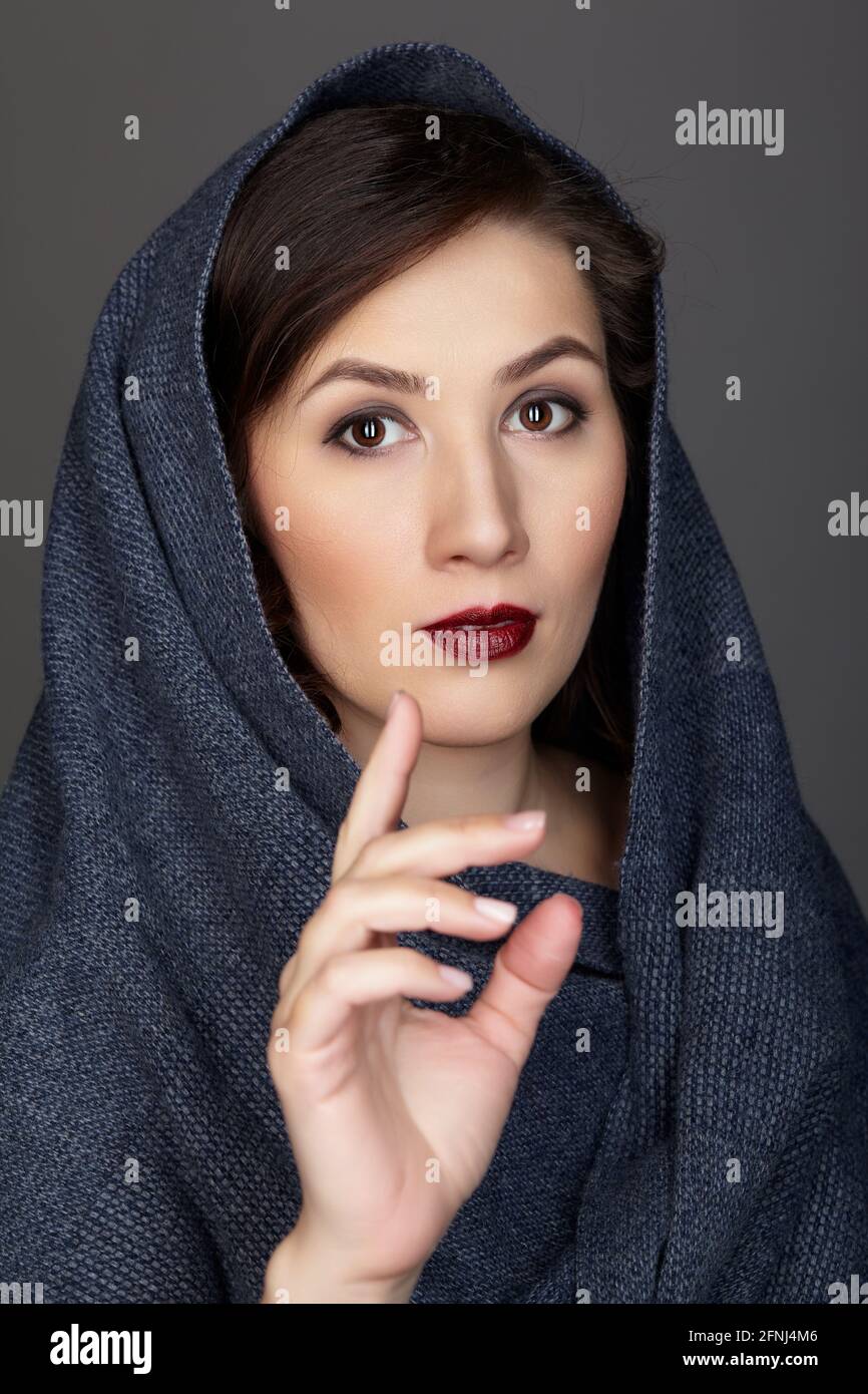 Portrait de beauté de la femme brune vêtue d'un foulard bleu foncé. Portrait de femme avec un angle de trois quarts sur fond noir. Main devant le visage. Banque D'Images