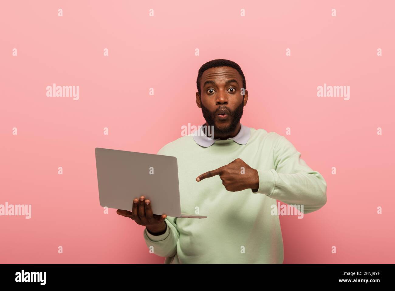 surpris afro-américain homme pointant vers l'ordinateur portable sur fond rose Banque D'Images