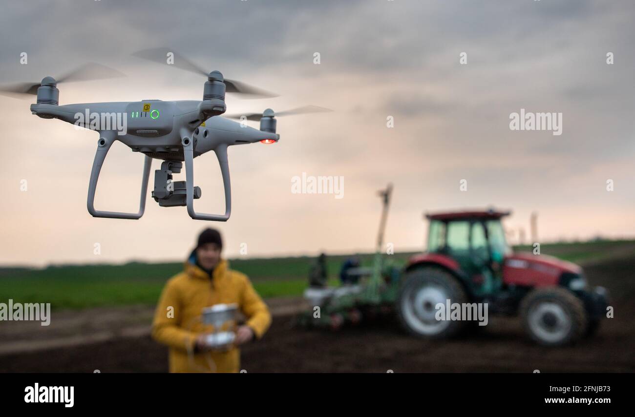Agriculteur conduisant un drone au-dessus du champ avec un tracteur qui sème le sol Banque D'Images