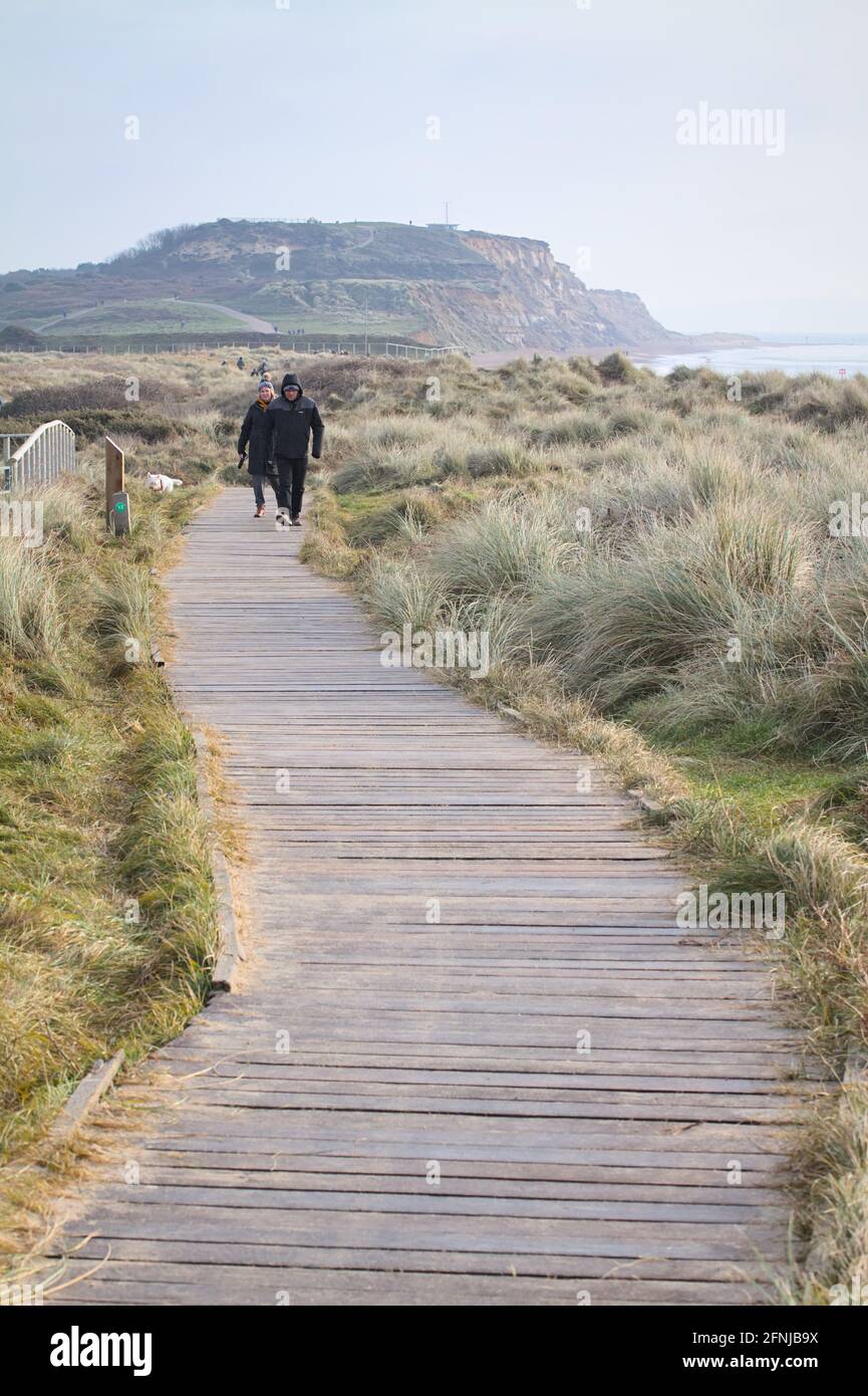Deux personnes marchant sur UNE promenade en bois à travers Sand Dunes avec Warren Hill, Hengistbury Head in the Background, hiver Royaume-Uni Banque D'Images