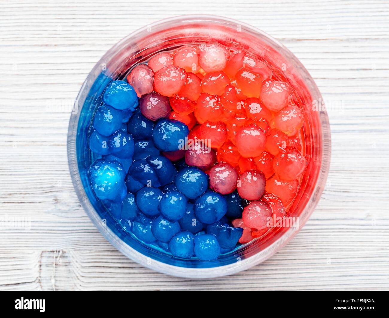 vue de dessus des bulles de tapioca bouillies rouges et bleues dans un bol en verre sur une table en bois gris Banque D'Images