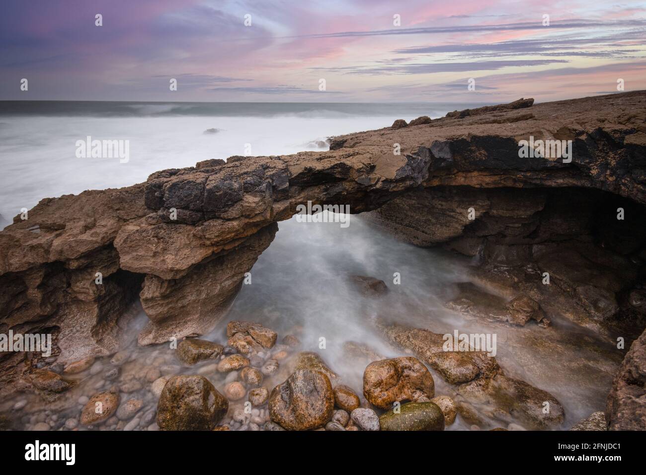 Formation rocheuse en forme d'arche sur la côte au coucher du soleil. Exposition longue Banque D'Images