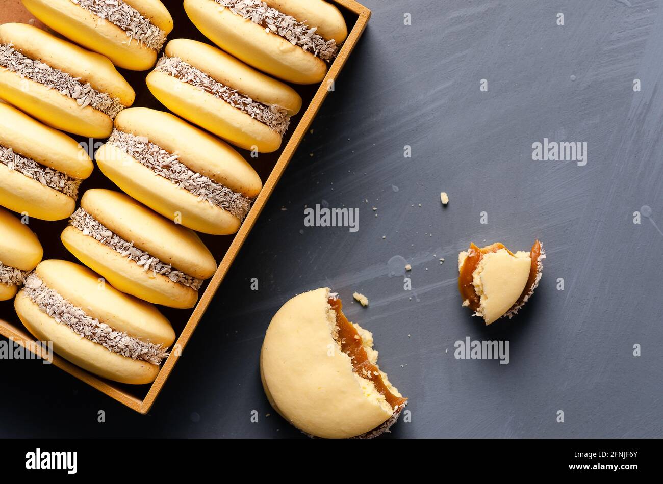 Fécule de maïs alfajores au caramel au lait et à la noix de coco dans une boîte en bois sur fond bleu clair. Banque D'Images