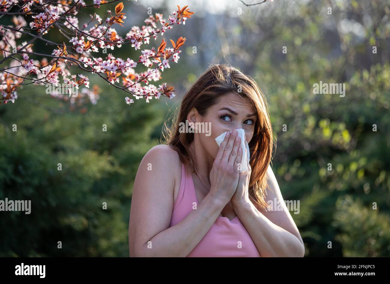 Jolie jeune fille soufflant le nez devant l'arbre en fleurs. Concept d'attaque contre les allergies aux pollens de printemps Banque D'Images