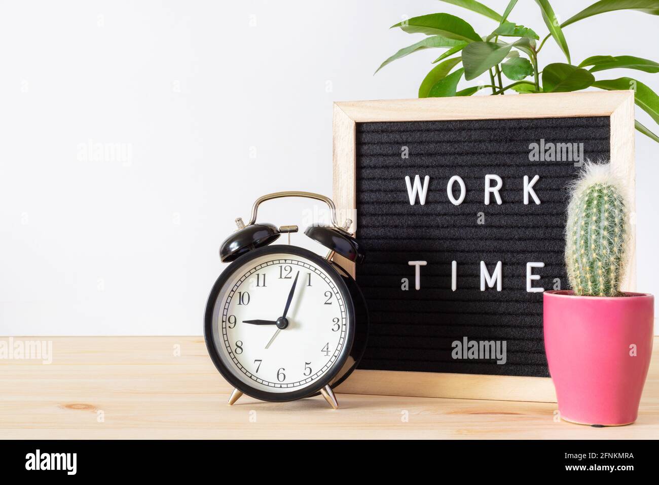 Réveil classique noir vintage, ordinateur portable, plantes en pot et panneau « Work Time » sur un bureau en bois avec fond de mur blanc et espace de copie pour le texte. Banque D'Images