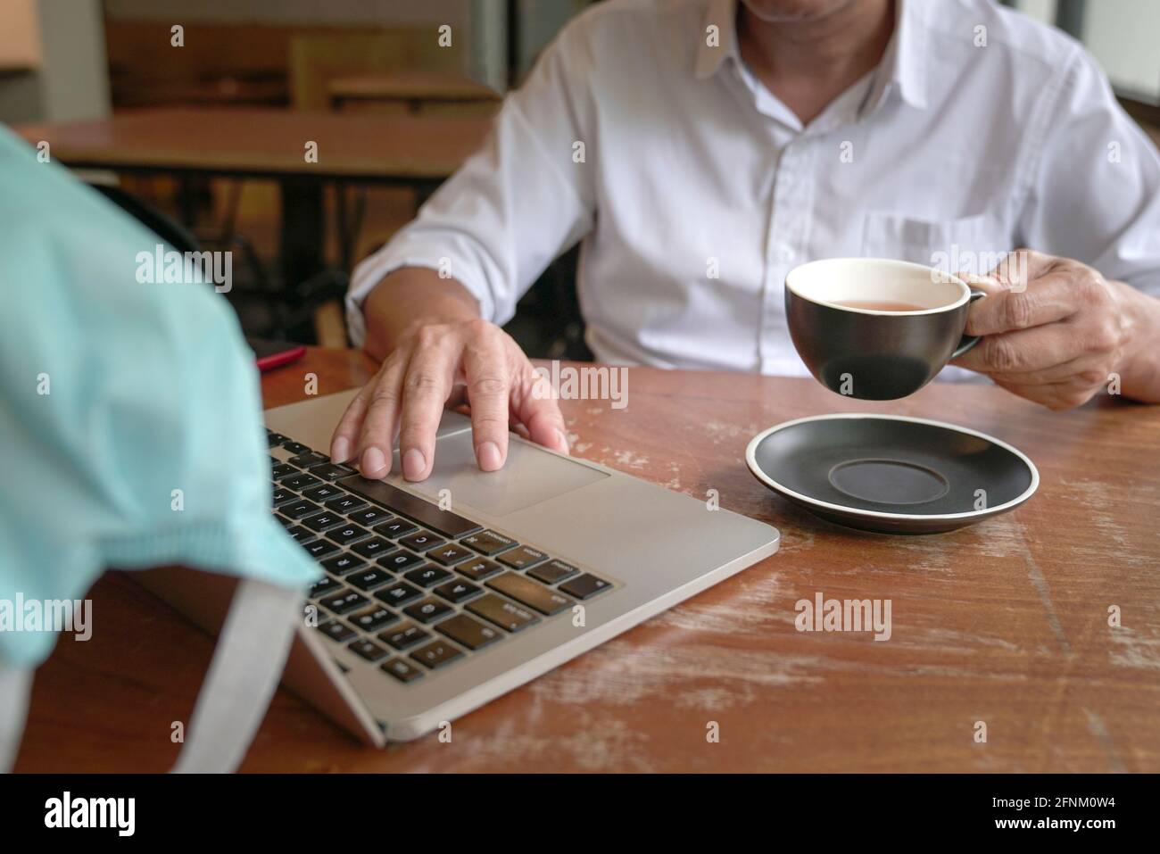 Homme d'affaires touchant le tapis de souris sur l'ordinateur portable et tenant une tasse de thé avec une autre main. Banque D'Images
