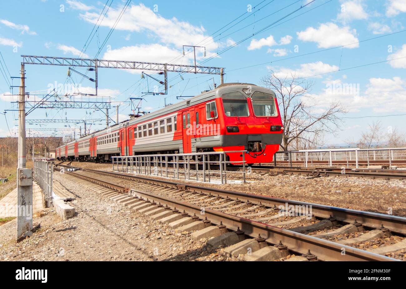 Un train électrique circule sur des voies ferrées rouillées contre un ciel bleu avec nuages blancs Banque D'Images