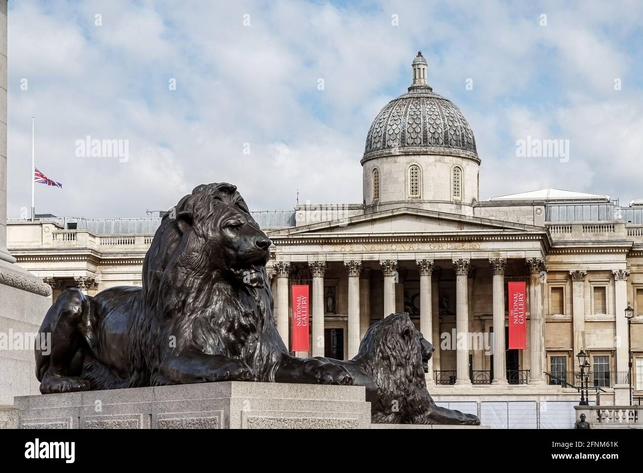 Deux lions de bronze à l'extérieur de la National Gallery, Trafalgar Square, avec le drapeau syndical volant à mi-mât. Banque D'Images
