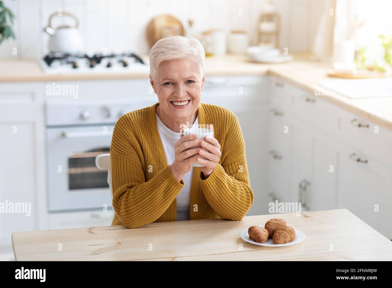 Bonne vieille dame prenant un café avec croissant Banque D'Images