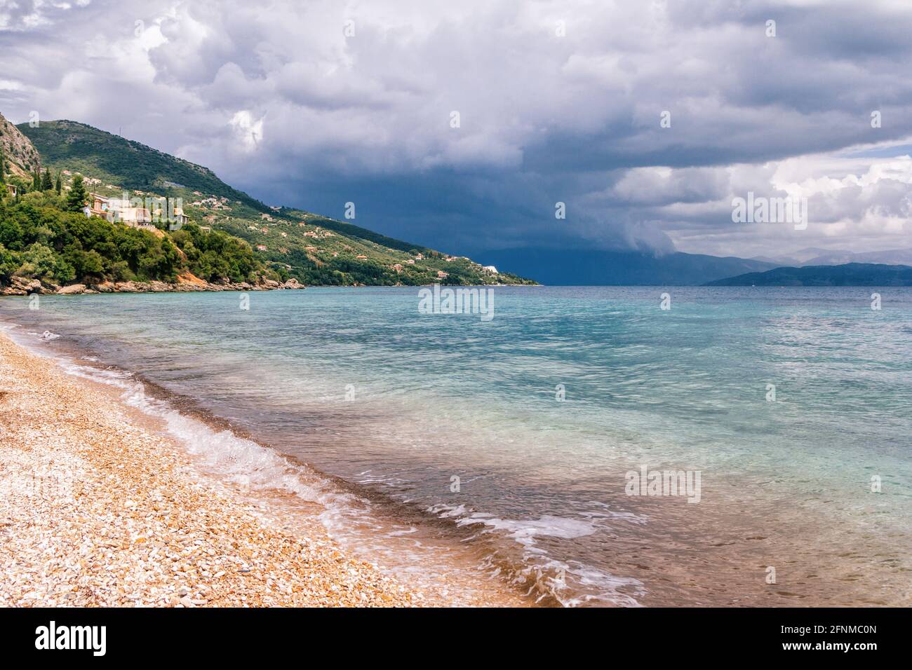 Beau paysage - turquoise couleur eau de mer, sable doré, ciel gris avec nuages sombres de tempête et montagnes à l'horizon. Banque D'Images